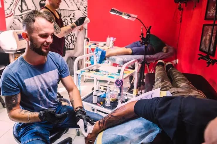 Tattoo artist wiping freshly tattooed arm of client 